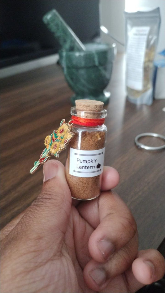 Hand holding a small bottle labeled 'Pumpkin Lantern' with a decorative tag.